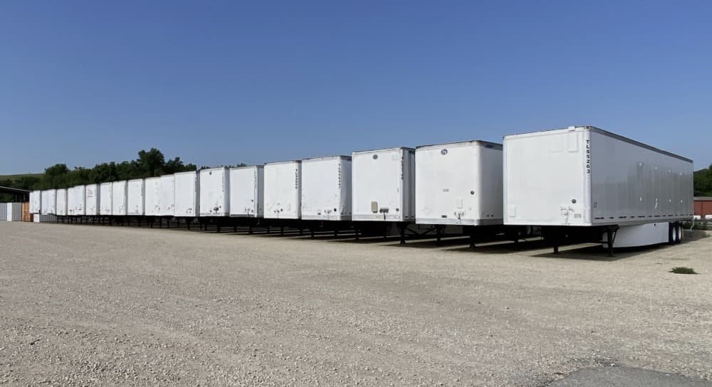 Row of white dry van storage trailers parked on a gravel yard